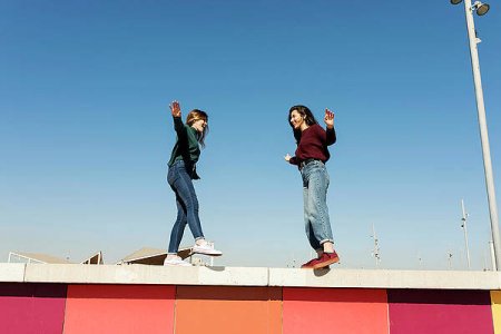 spain-barcelona-laughing-friends-walking-on-wall-at-sunlight-cavan-images.jpg
