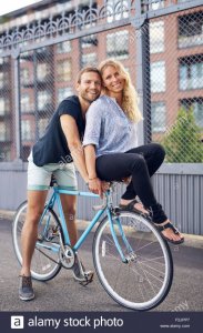 loving-couple-riding-bikes-woman-on-handlebar-F2JPP7.jpg